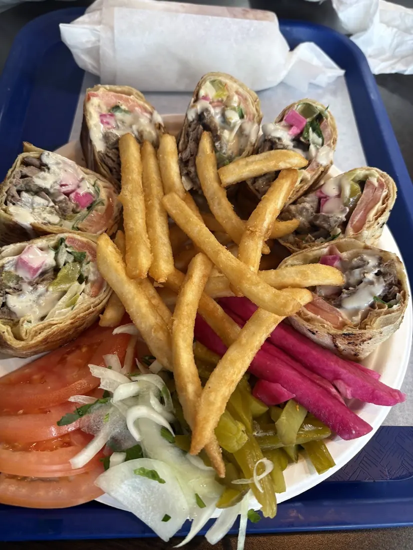 Shawarma plate with sliced meat wraps, fries, pickles, tomato and onion on a blue tray