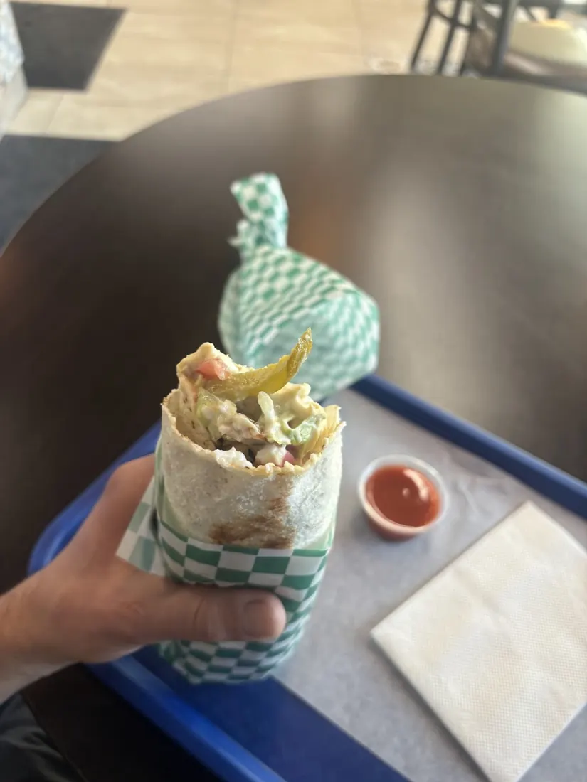 Hand holding a shawarma wrap in green and white checked paper