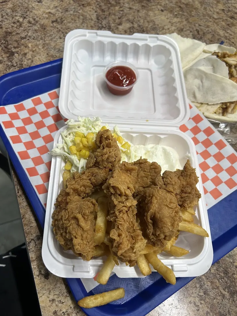 Crispy fried chicken pieces in a takeout box with a sauce cup